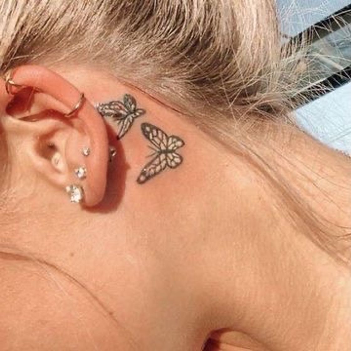 Social Tatuagem atrás da orelha com borboletas delicadas.