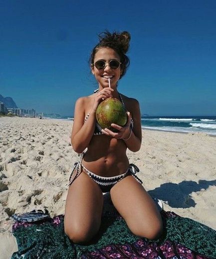 ajoelhada numa canga ou na areia com uma agua de coco